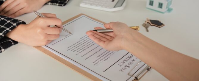 Woman signing a real estate contract with house keys nearby, representing tenant agreements and property management.